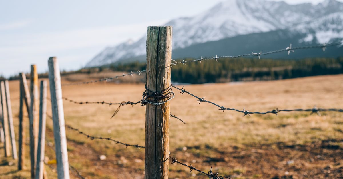 Cerca de alambre de púas en un potrero rural con montañas al fondo